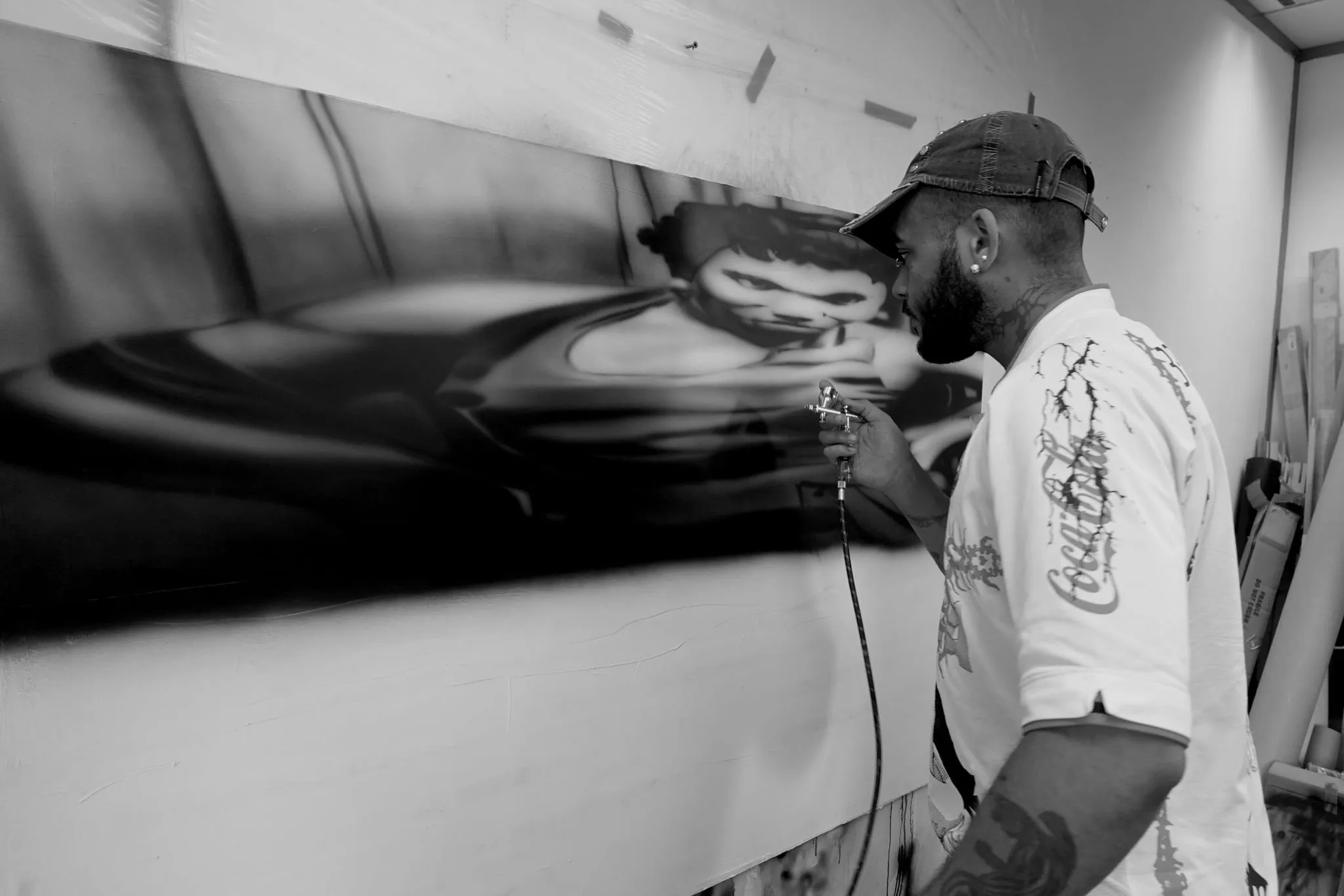 Mattia Guarnera-MacCarthy in profile, airbrushing the reclining-figure painting, wearing a Rizla-branded shirt