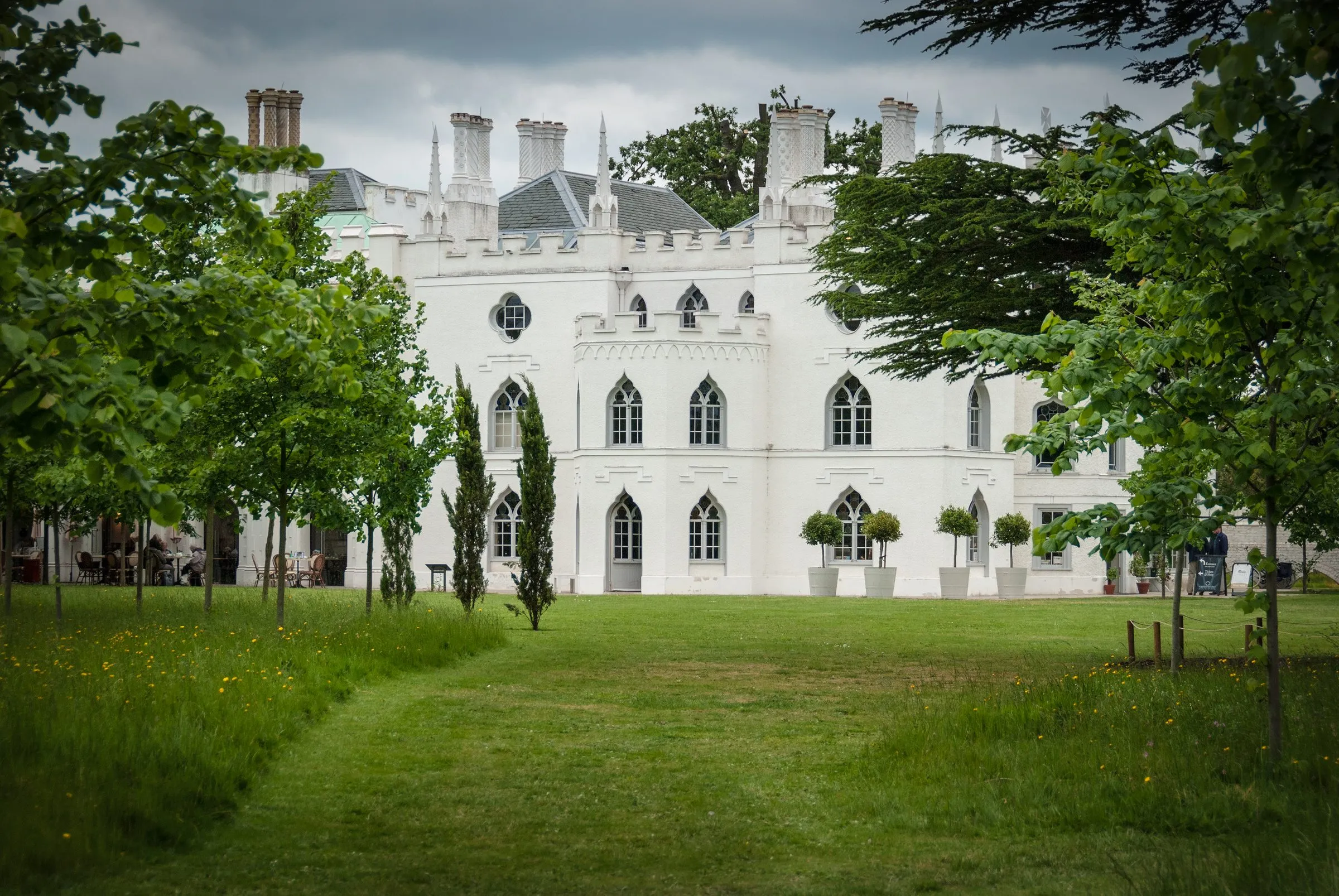 The white Gothic Revival garden front of Strawberry Hill House, with pinnacles, battlements and pointed-arch windows, seen across the lawn between young trees