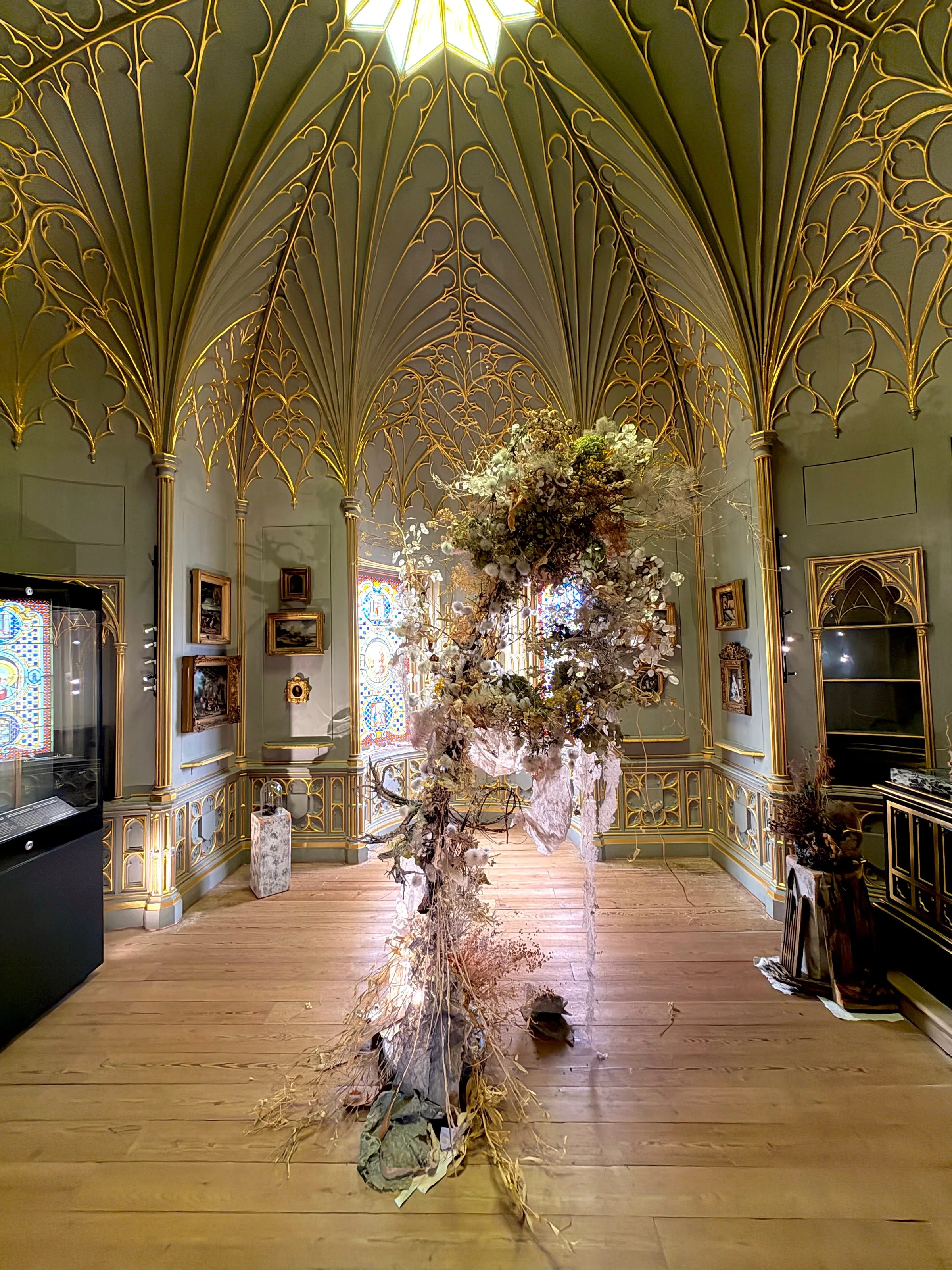 A suspended dried-flower installation hanging beneath a green and gilt fan-vaulted ceiling during the flower festival