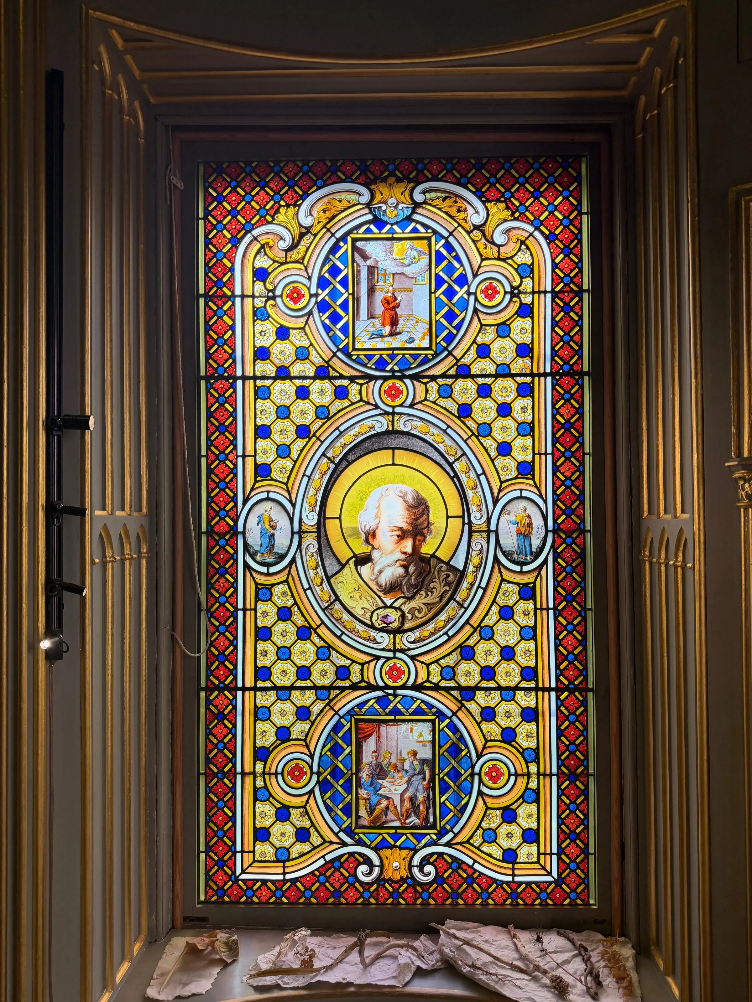 A tall stained glass window of saints in roundels, set in a gilded Gothic recess