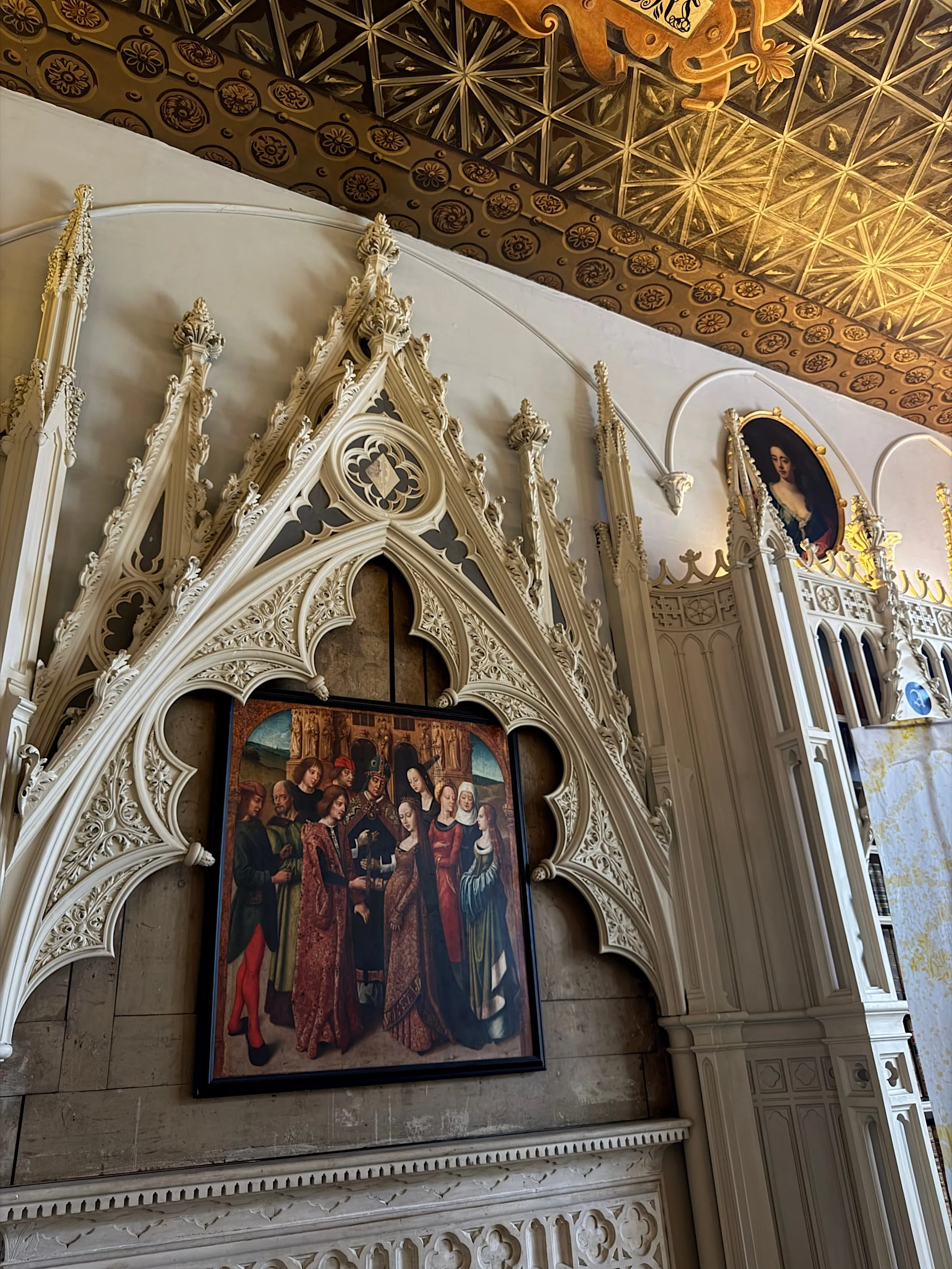 Carved white Gothic tracery framing an early Netherlandish painting beneath a gilded ceiling